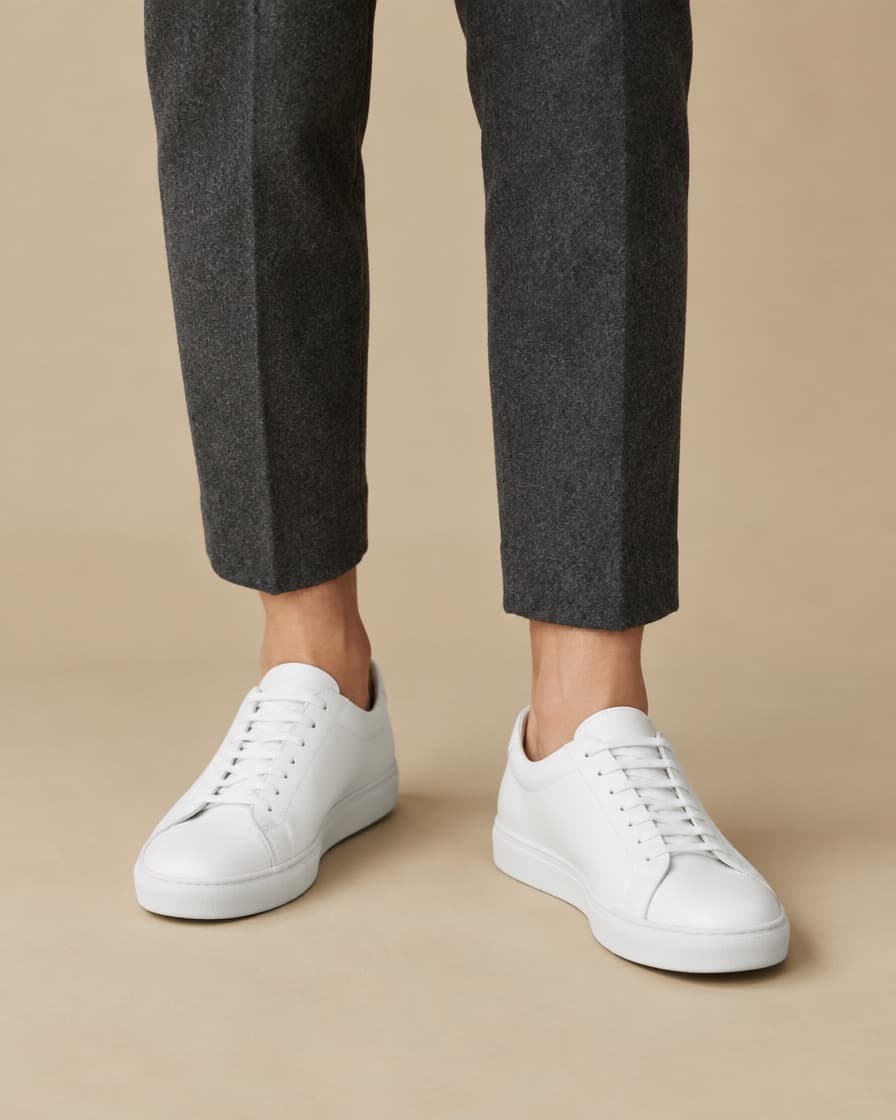 White leather sneakers worn with cropped charcoal trousers, seen from knee height